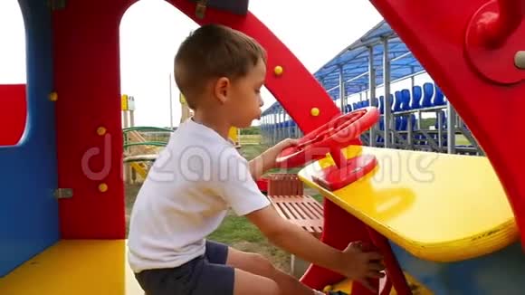 这个男孩坐在操场上的一辆木车里玩摄像机监视坐在玩具车里的孩子视频的预览图