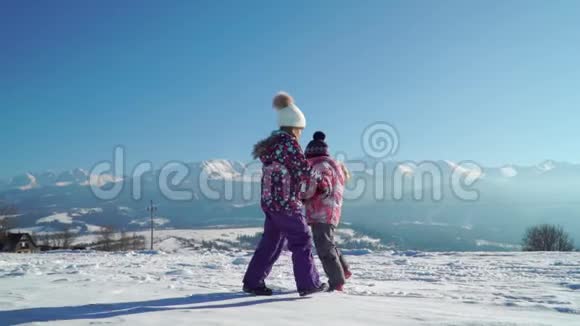 穿着户外服装的孩子们在雪地上奔跑阳光下背景着美丽的山脉视频的预览图