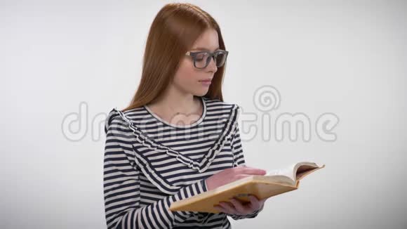 年轻甜美冷静的戴着眼镜的姜姑娘正在看书看着镜头微笑着白色的背景视频的预览图