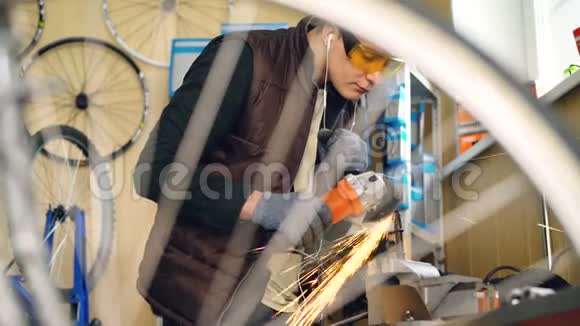忙碌的年轻人熟练的修理工正在使用小金属部分的电动圆锯自行车备件和不错的视频的预览图