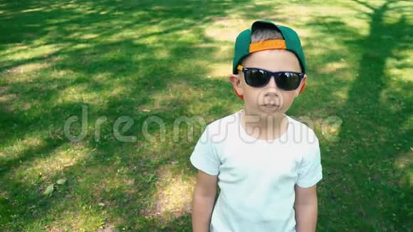 一个5岁的小男孩戴着太阳镜站在夏天的公园里开始微笑这是孩子真正的情感视频的预览图