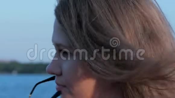 美丽微笑的白种人女孩在夕阳下戴上太阳镜模糊的背景视频的预览图