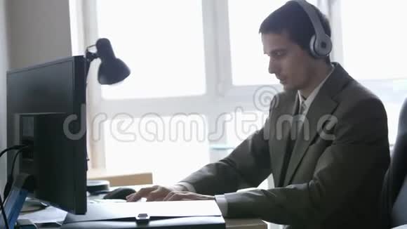 成功的商人戴着耳机坐在办公桌前在全景窗口的电脑上工作3840x2160视频的预览图