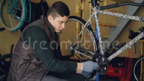 熟练的年轻人职业机械师正在他工作场所的地板上用钥匙固定自行车踏板视频的预览图
