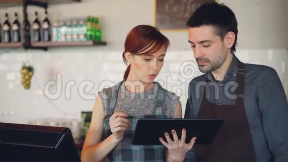 有魅力的年轻人咖啡屋老板在柜台边工作边使用平板电脑和聊天伙伴关系视频的预览图