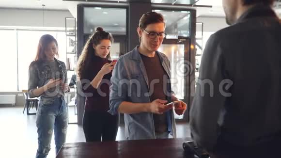 咖啡馆里的快乐顾客正在用智能手机付款而排队的顾客正在等待和使用手机视频的预览图
