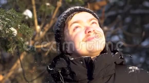 年轻的微笑的留着小胡子的男人的画像在冬天的森林里享受着降雪的乐趣从他的眼睛里眯起视频的预览图