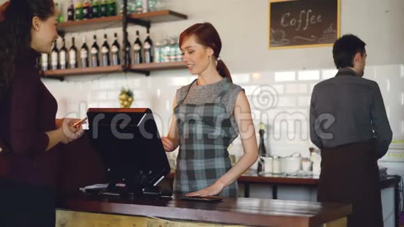 漂亮的现代咖啡馆的礼貌微笑的员工在出售外卖饮料而快乐的顾客则在付钱视频的预览图