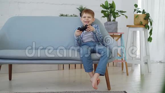快乐的小孩独自玩电子游戏坐在家里的沙发上玩得很开心现代技术快乐的童年视频的预览图