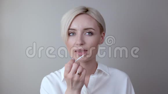 一个留着短发的年轻金发女孩直接看着相机用魔杖涂抹唇膏视频的预览图