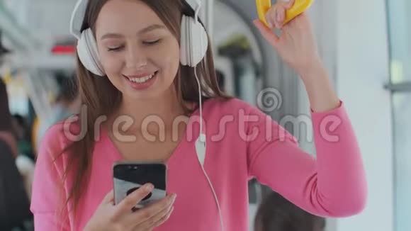 年轻女性乘客戴着耳机和智能手机站在现代有轨电车上享受旅途中的乐趣视频的预览图
