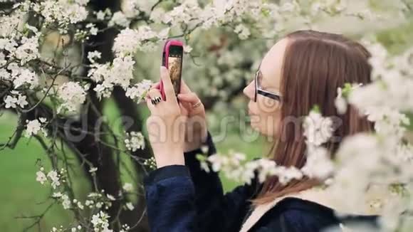 美丽的女孩在智能手机上拍摄春天的花朵视频的预览图