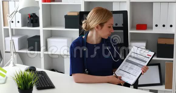 医生坐在办公椅上在文件中显示笔记看着相机视频的预览图