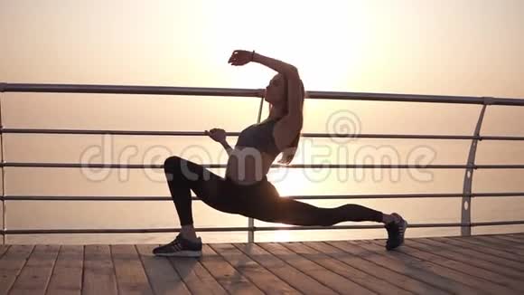 长发女孩穿着运动服伸展腿部肌肉做弓步在横梁上倾斜早晨的太阳视频的预览图