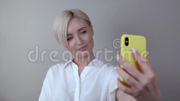 可爱的短发金发女孩为自拍做特写女人在黄色的箱子里用手机自拍视频的预览图