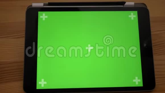 水平平板电脑的远程特写镜头木制桌子背景上有绿色屏幕视频的预览图