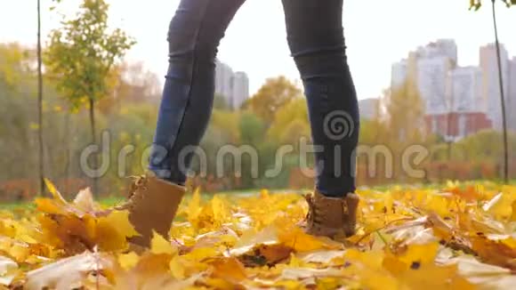 在黄色落叶的公园里穿靴子行走的女人腿特写视频的预览图