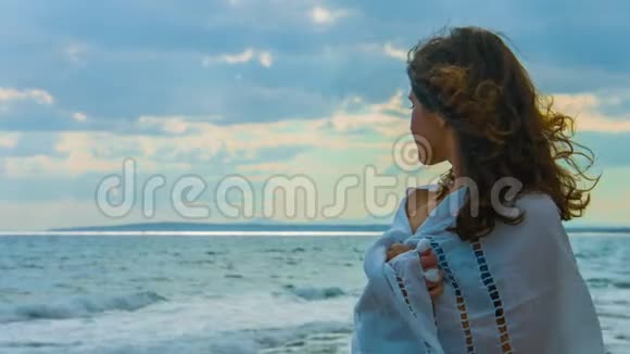孤独的美丽女人戴着围巾站在海边看着暴风雨视频的预览图
