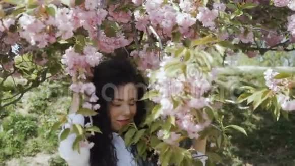 微笑的黑发女人触摸盛开的树枝看着镜头慢镜头视频的预览图