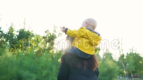 日落时分妈妈和她的孩子在公园里玩男孩穿着一件黄色夹克坐在他的肩膀上开心地笑着视频的预览图