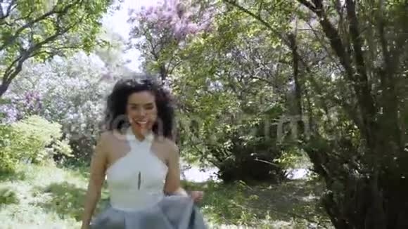 一位美丽的笑着的黑发女郎在镜头前穿过一个夏日花园视频的预览图