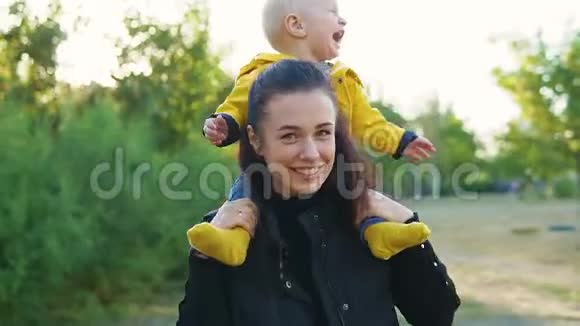 日落时分妈妈和她的孩子在公园里玩男孩穿着一件黄色夹克坐在他的肩膀上开心地笑着视频的预览图