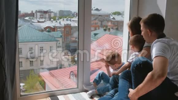 家庭妈妈爸爸和两个双胞胎兄弟蹒跚学步的孩子看着窗外的城市视频的预览图