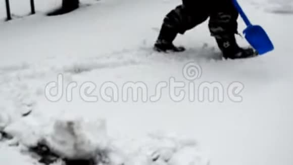 快乐的小男孩穿着冬季连衣裙玩着塑料铲子在冬季公园的雪道上擦雪视频的预览图