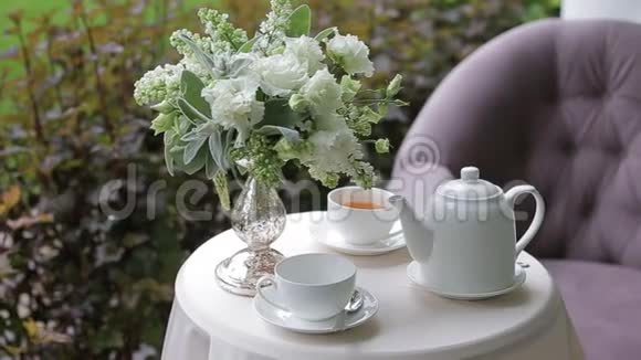 在户外的一张白色桌子上摆着一束鲜花上面放着白色杯子里的热茶视频的预览图