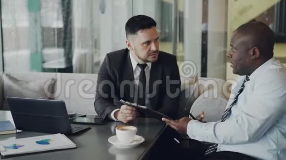 两个野心勃勃的商业伙伴看着他们的合同在他们的桌子上唱着手提电脑和图表视频的预览图