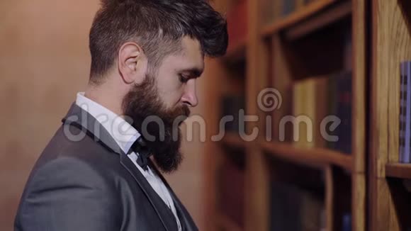 那个留胡子的人站在图书馆的书架前看一本书读书的观念视频的预览图