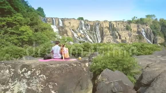 近景后景男女孩坐在石表瀑布视频的预览图