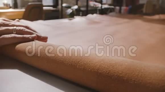 男工手工的特写镜头将一大块棕色皮革卷成制造车间桌上的卷轴视频的预览图