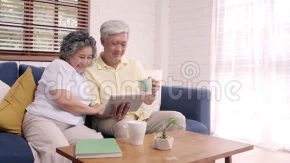 亚洲老年夫妇在家里的客厅里使用平板电脑和喝咖啡视频的预览图