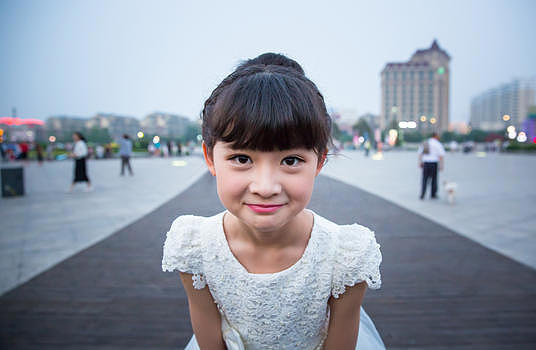 傍晚小姑娘穿着白裙站在广场上露出特殊的表情图片素材免费下载