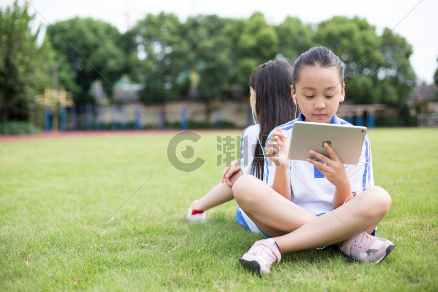坐在草坪上使用平板电脑的小学生图片素材免费下载