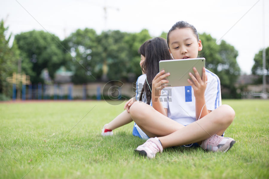 坐在草坪上使用平板电脑的小学生图片素材免费下载