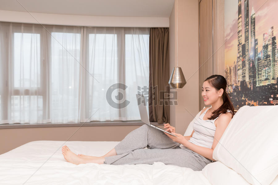 坐在床上玩电脑休闲放松的年轻女性图片素材免费下载