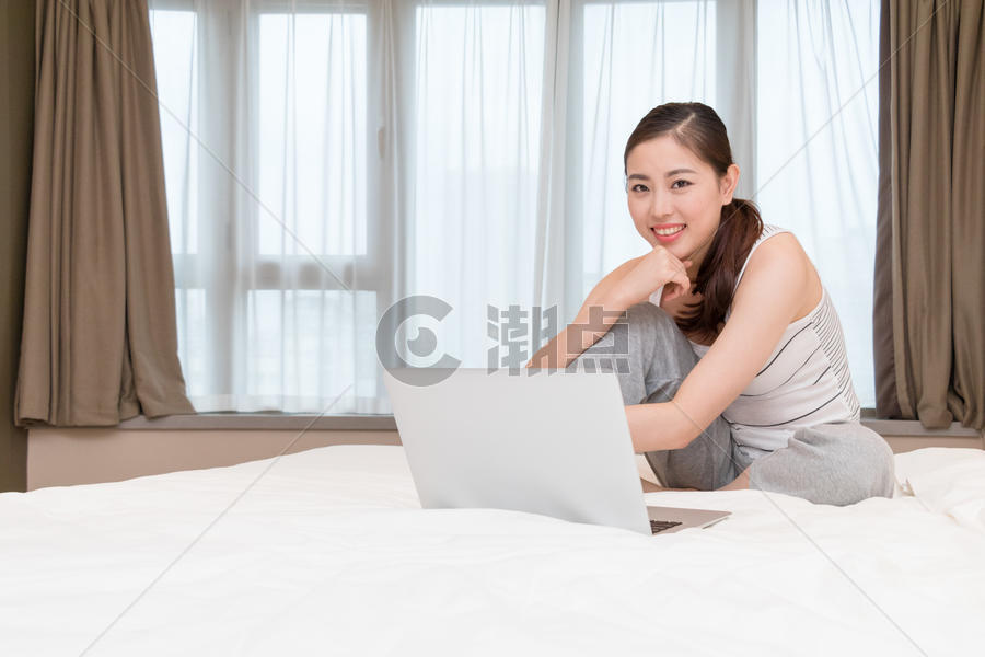 坐在床上玩电脑休闲放松的年轻女性图片素材免费下载