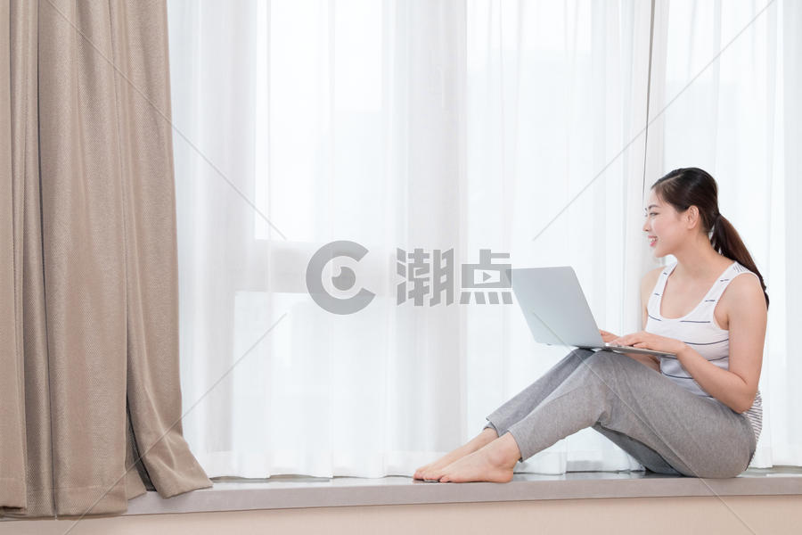 坐在客厅窗台使用笔记本电脑的美女图片素材免费下载