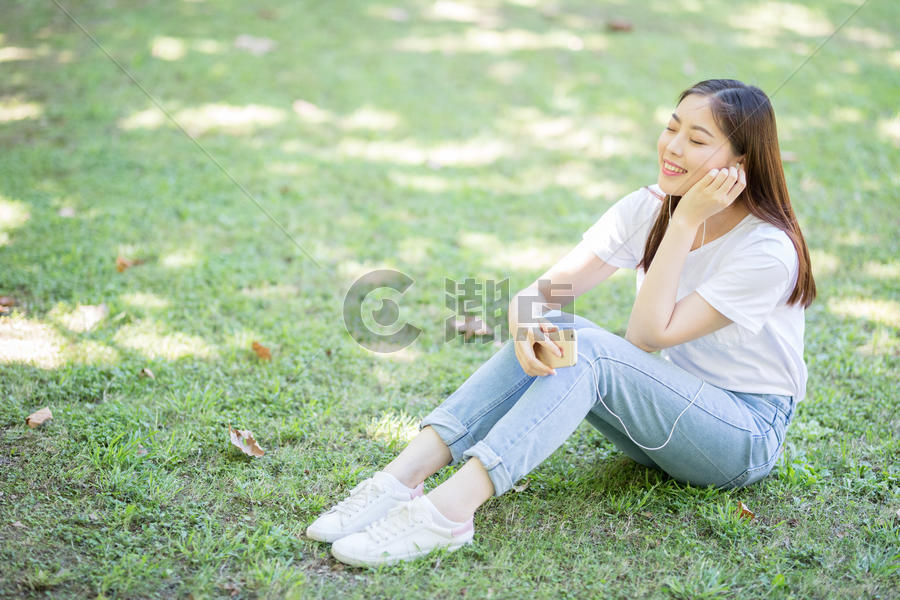 校园草坪上看手机听音乐的女生图片素材免费下载