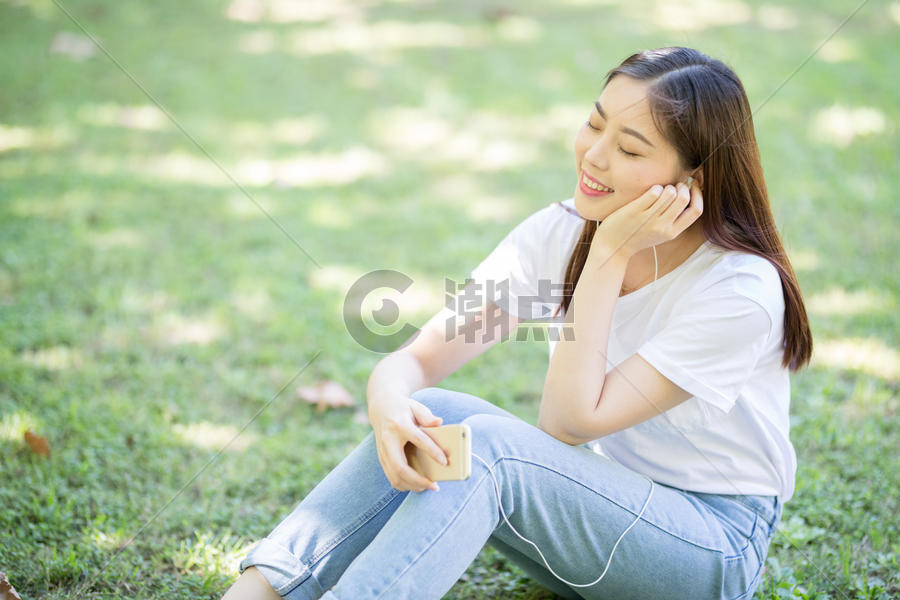 校园草坪上看手机听音乐的女生图片素材免费下载