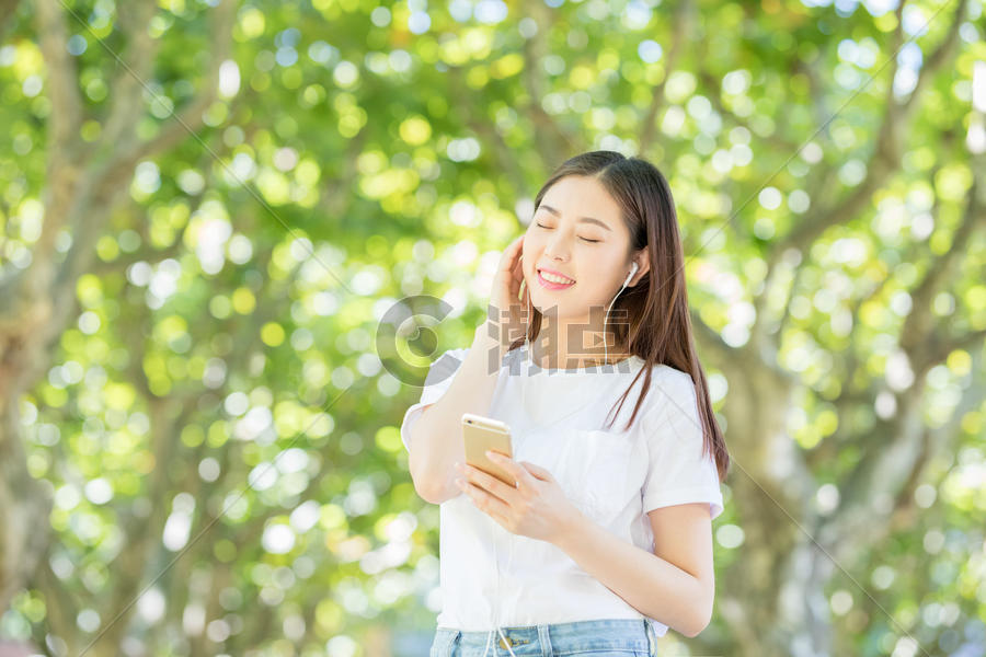 树林下戴耳机听音乐的甜美女生图片素材免费下载