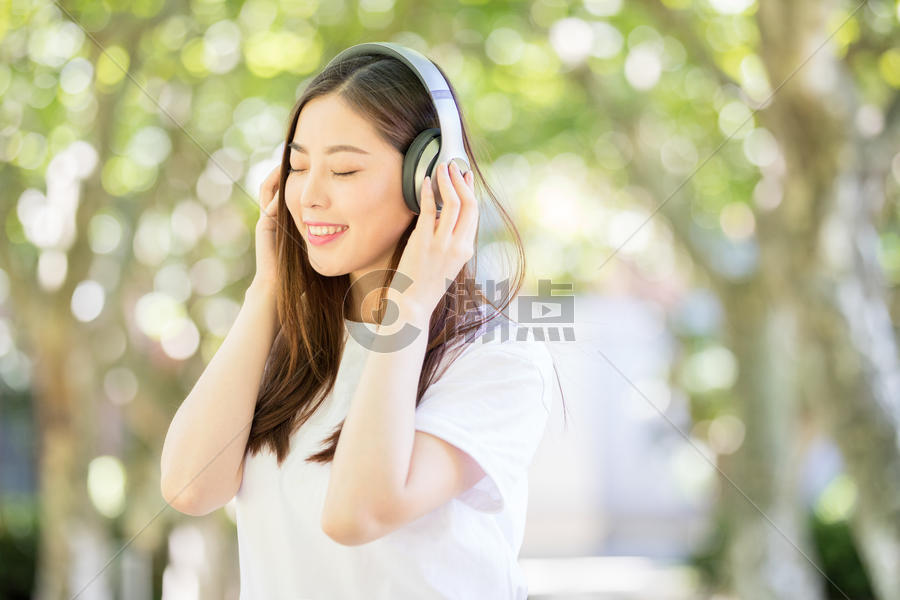 树林下戴耳机听音乐的甜美女生图片素材免费下载