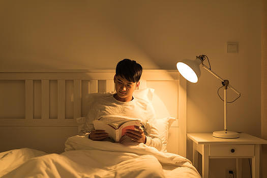 晚上坐在床头看书的年轻男性图片素材免费下载