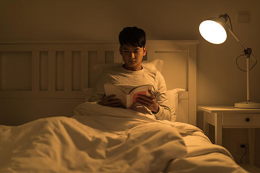 晚上坐在床头看书的年轻男性图片素材免费下载