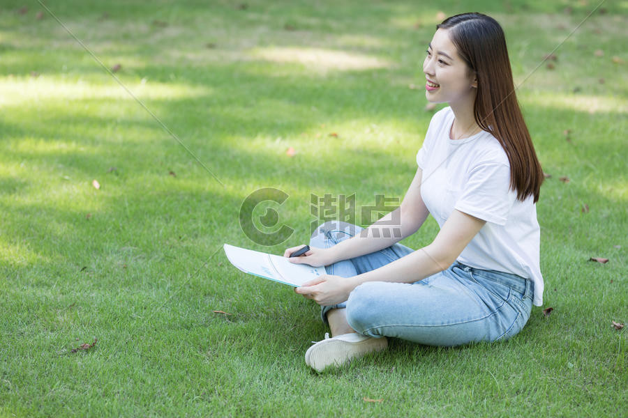 拿着课本坐在草坪上看书的大学生图片素材免费下载