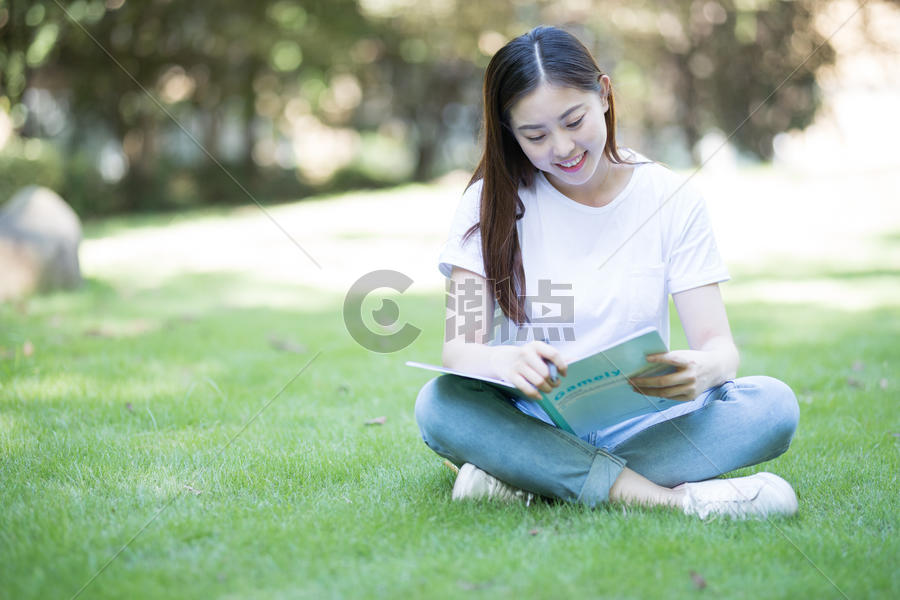 拿着课本坐在草坪上看书的大学生图片素材免费下载