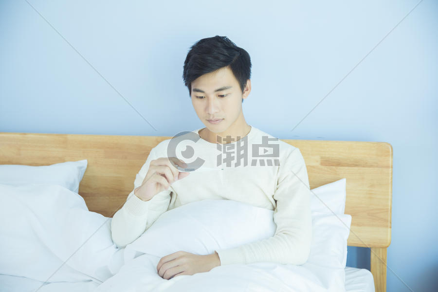 躺床上测量体温的年轻男性图片素材免费下载