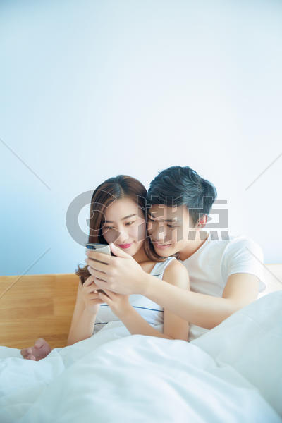 年轻情侣在床上看手机图片素材免费下载